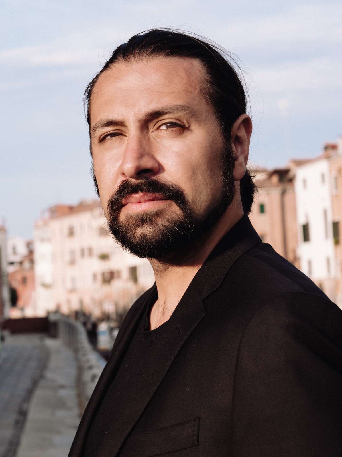 Editorial portrait of Francesco Bossaglia, direct gaze at camera in golden-hour light, Venice architecture softly blurred behind.