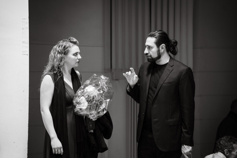 Black-and-white photo of Francesco Bossaglia backstage after a concert, in conversation with a soloist holding a bouquet.